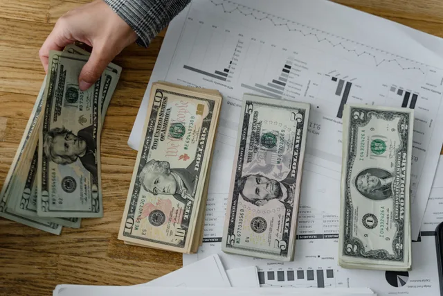 Person holds US dollars over financial papers, showing income or budget analysis. Implementing payroll software with reconciled migration, parallel runs and a rehearsed cutover