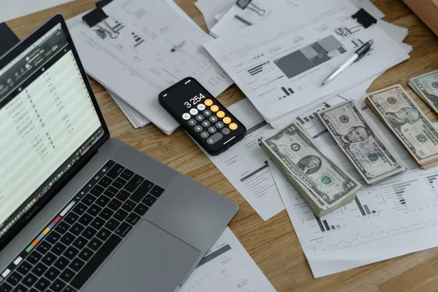 A desk with financial documents, currency, a laptop, and phone calculator. Payroll software checks in England: PAYE, pensions and UK GDPR